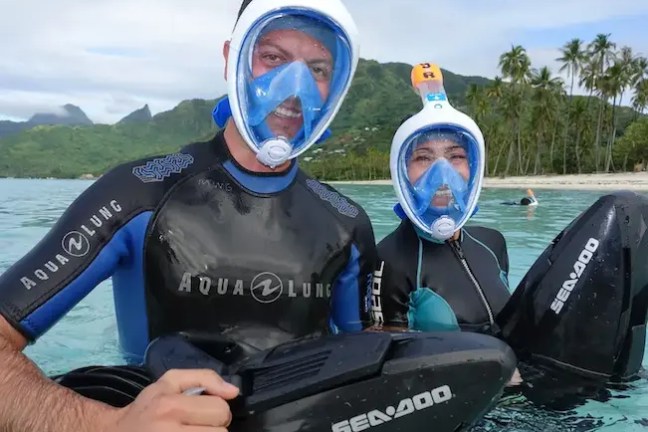 Happy couple enjoying a sea scooter jet snorkeling adventure in Moorea lagoon turquoise water.