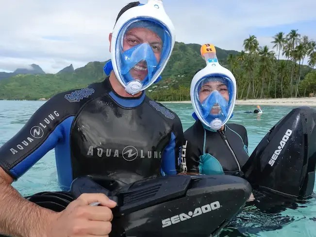 Happy couple enjoying a sea scooter jet snorkeling adventure in Moorea lagoon turquoise water.